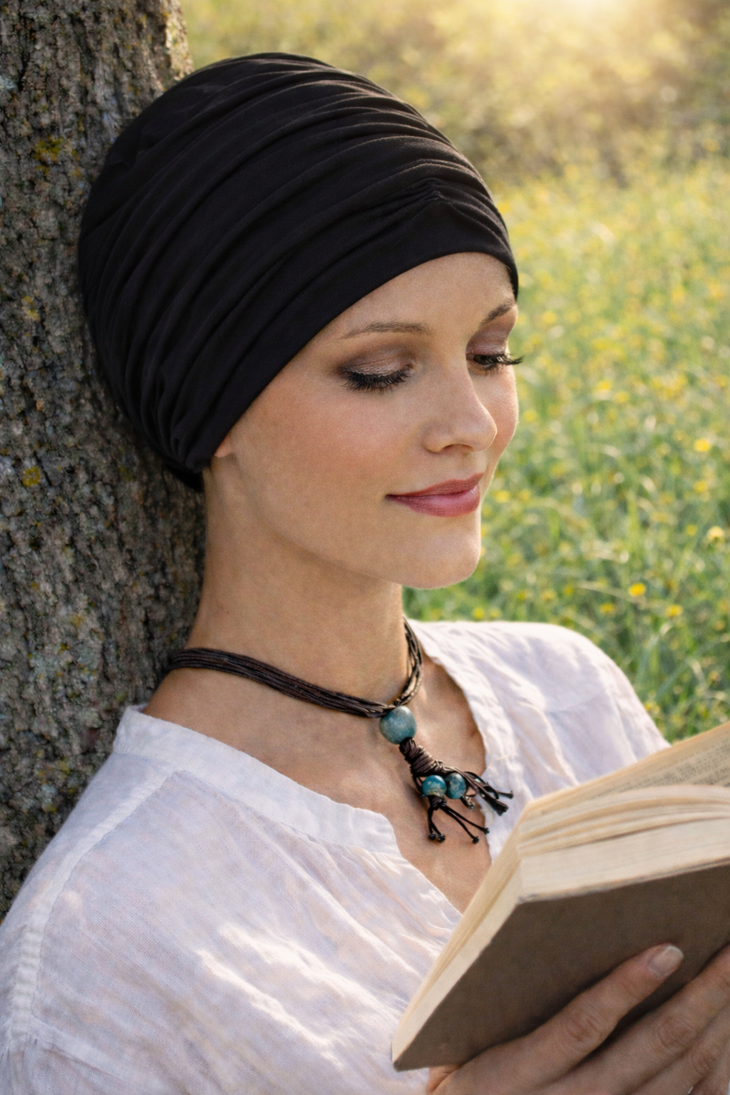Frau mit schwarzem Turban lehnt an einem Baum auf einer Wiese